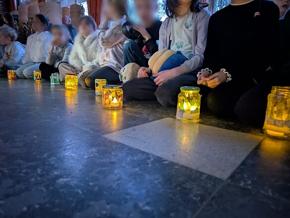 Kinder sitzen auf dem Boden, vor sich Adventslichter